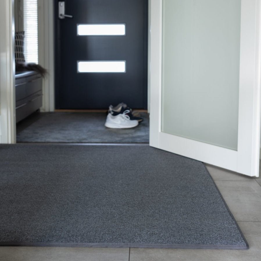 Keskiharmaa eteisen matto laattalattian päällä.